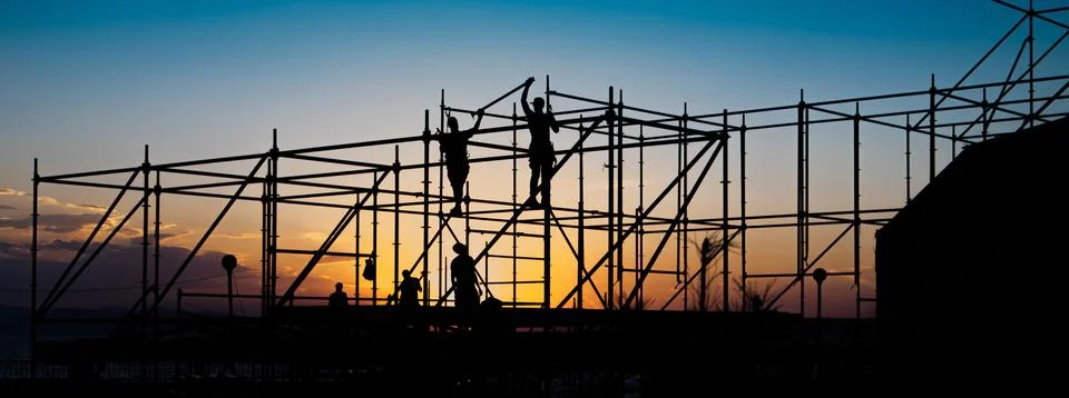 Construction workers working on scaffolding. Figures on a sunset. Stock Photos