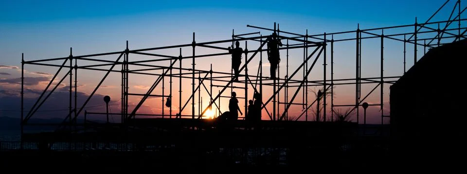 Construction workers working on scaffolding. Figures on a sunset. Stock Photos