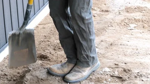 Construction working man uses a flat shovel to scrape brown dirt by a wall. Stock Footage 154869682