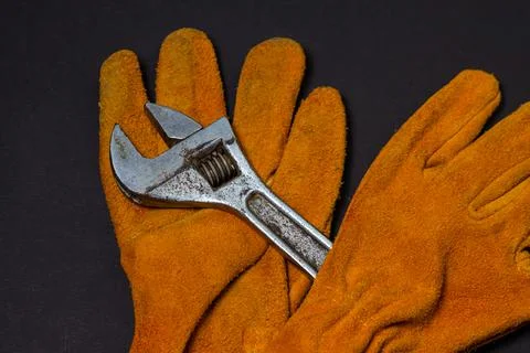 Construction yellow gloves and an adjustable wrench on a black background.  Stock Photos
