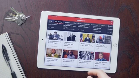 Consumer reading BBC News app on Apple iPad at home Stock Footage 75460458