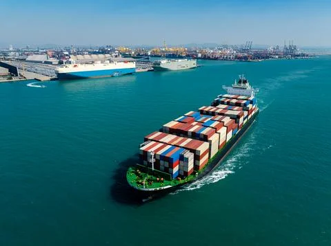 Container Cargo Ship Navigating In Turquoise Harbor Waters Toward Port Term.. 스톡 사진