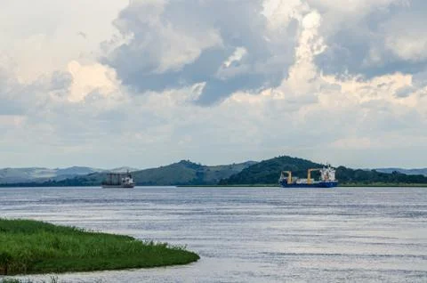 Container cargo ships on mighty Congo river with dramatic cloudy sky and lush Stock Photos