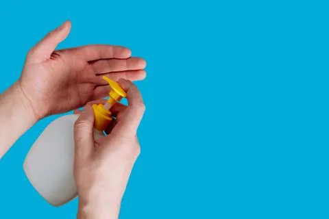 Container with liquid soap and hands on a blue background. Disinfection durin Stock Photos