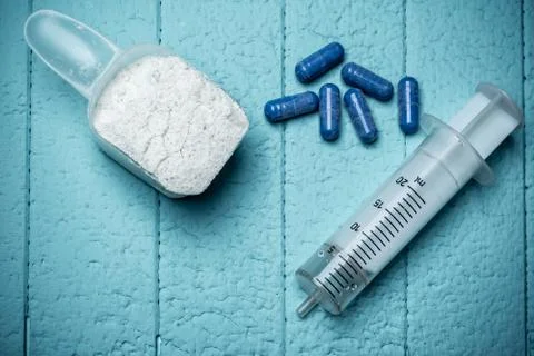 Container of milk whey protein, empty injection and pills. Close-up. Blue Stock Photos