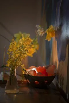 Container with rocks and light illuminating a vase with yellow flowers Stock Photos