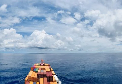 Container Ship Bow Sailing Across Calm Ocean Beneath Dramatic Tropical Clouds Stock Photos