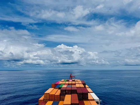 Container Ship Carrying Cargo Containers Across Calm Ocean Under Dramatic Cloudy Foto stock