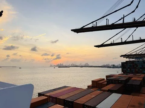 Container ship deck cargo with cranes at sunset approaching a harbor Stock Photos