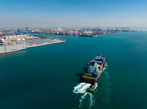 Container Ship Escorted By Tugboats Navigating Harbor Waters At Shipping Te.. 库存照片
