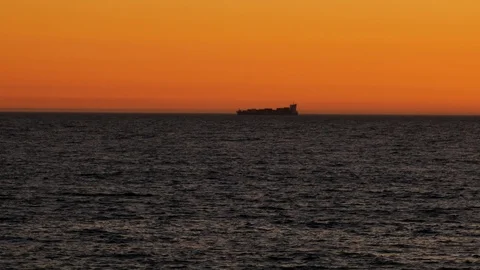 Container ship on horizon at dusk on ocean, silhouetted against the orange sky Stock Footage 108946156