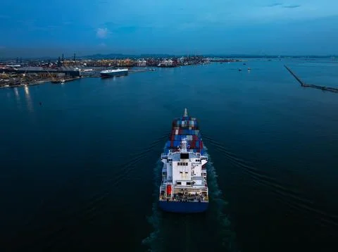 Container Ship Navigating Through Bustling Industrial Port At Twilight Bird.. 스톡 사진