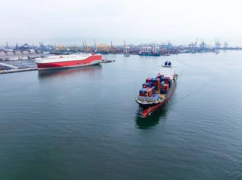 Container Ship Navigating Through A Busy Industrial Harbor Wide Shot Stock Photos