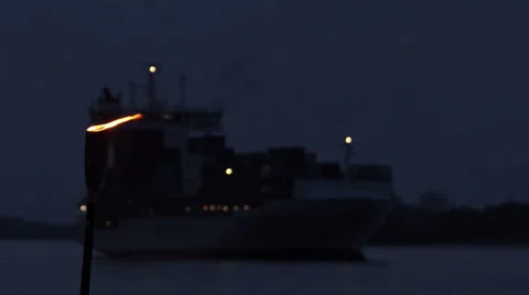 Container ship at night passing by and a torch with fire on a shore Stock Footage 67676285