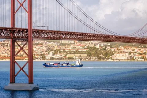 Container ship passing under 25 de Abril bridge, Lisbon, Portugal on sunny day Stock Photos