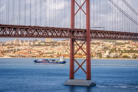 Container ship passing under 25 de Abril bridge, Lisbon, Portugal on sunny day Foto stock