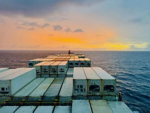 Container Ship Sailing at Sunset Across Open Sea with Cargo Containers and Drama Foto stock