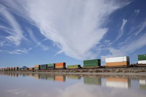 Container stack train reflected in standing water under cloudy sky Stock Photos