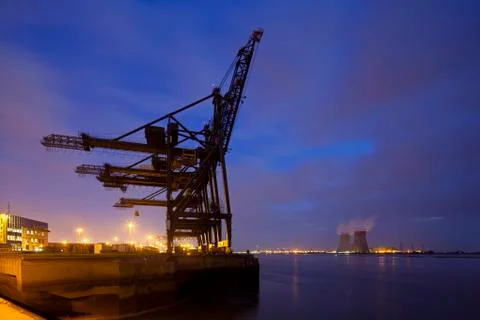A container terminal with tall cranes with a nuclear power station in the bac Stock Photos