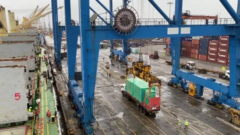 Container unloading from a vessel onto a flatbed trailer at a busy cargo Stock Footage 345210188