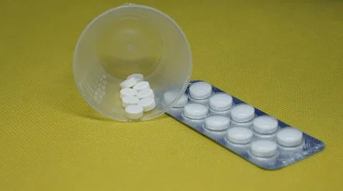 A container with white medical pills next to a package of white pills 写真素材