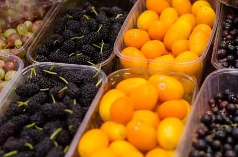 Containers with different ripe berries and fruit at market Stock Photos