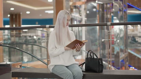 Contemplative customer reading book on mall bench Stock Footage 316849913