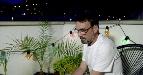 A contemplative man sits on a balcony at night. Stock Footage 336310856