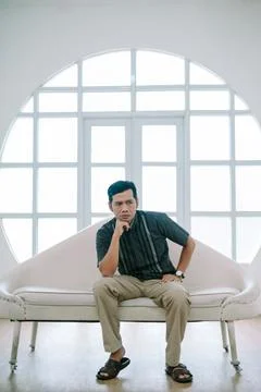Contemplative man sitting on sofa in front of an arched window Stock Photos