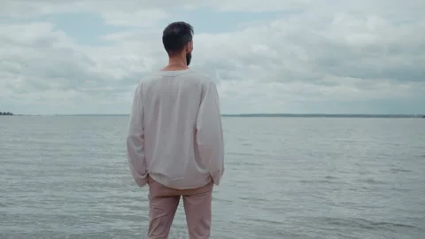 Contemplative man standing alone on a deserted beach Stock Footage 328559304