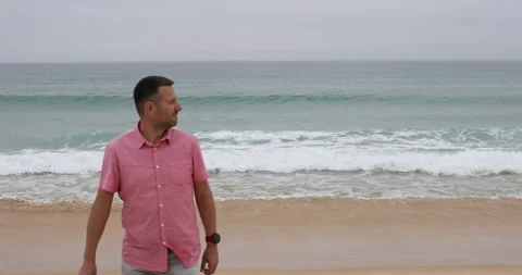 Contemplative Man Walking Along Misty Beach with Turquoise Ocean Waves Stock-Footage 310732965
