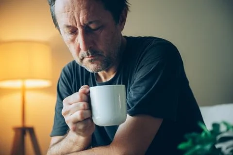 A contemplative middle-aged man drinking from a coffee mug in warm living r.. Stock Photos