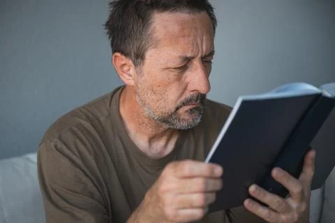 Contemplative middle-aged man reads a book with a focused, thoughtful expre.. Stock Photos