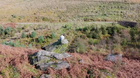 A contemplative young boy rests on a sizable rock outcrop, lost in thought,.. Видео 254160688