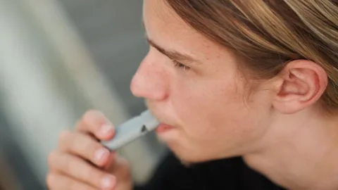 Contemplative young man enjoys vaping during study break outside. Young male Stock Footage 334946635