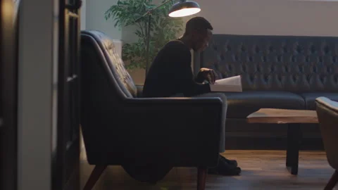 A Contemplative Young Man in Glasses Sits on a Couch and Reads Holy Scriptures Stock Footage 208750027