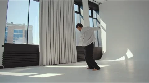 Contemporary dancer leaning forward in bright minimalist studio with barefoot Stock Footage 345248771