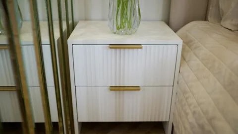 Contemporary white bedside table with ribbed drawers and gold hardware. Glass Stock Photos