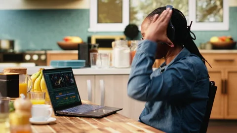 Content creator editing video footage on laptop with headset Stock Footage 344246278