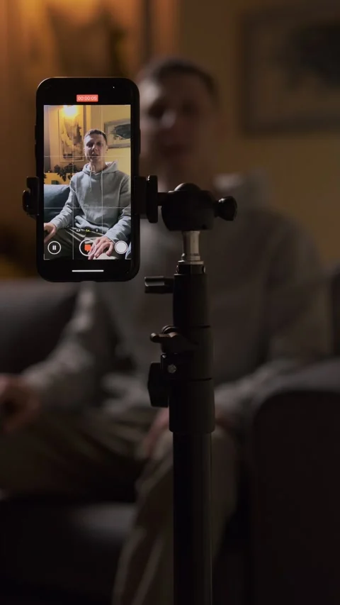 Content creator pressing record button on smartphone, sitting on couch and Stock-Footage 314893615