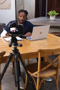Content creator is sitting at wooden dining table with DSLR on tripod and open Stock Photos