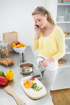 Content cute blonde phoning while preparing a meal Stock-Fotos
