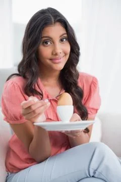 Content cute brunette sitting on couch holding hard boiled egg 스톡 사진