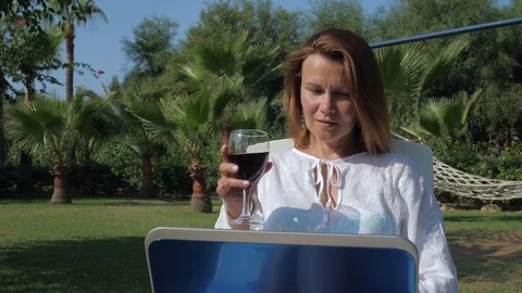 Content female freelancer using laptop with glass of wine on vacation Stock Footage 124594526