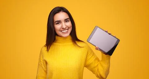 Content Hispanic lady showing tablet and smiling in yellow studio Stock Photos