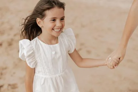 Content kid smiling while holding hand of crop mom on sandy seashore Stock Photos