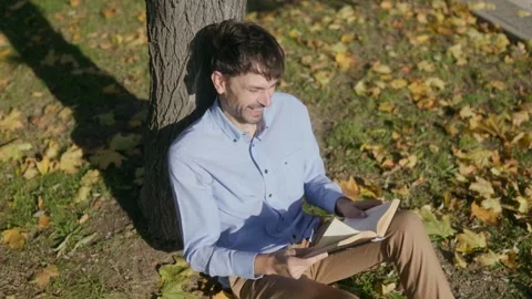 Contented Reader Enjoying a Sunny Day and a Good Book by a Tree Stock Footage 300250413