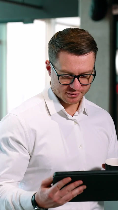 Continuing work during the coffee break. Man is focused on I-pad holding a paper Stock Footage 320886502