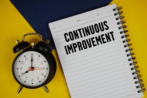 Continuous Improvement text written on notepad with alarm clock on yellow b.. Stock Photos