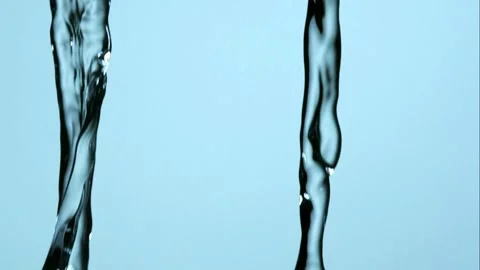 A continuous stream of clear water pours down against a light blue background Stock Footage 326628556
